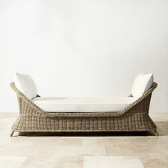 a wicker chaise lounger with white cushions on a tile floor in front of a wall