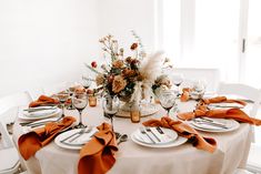 the table is set with white plates and silverware, orange napkins, and flowers