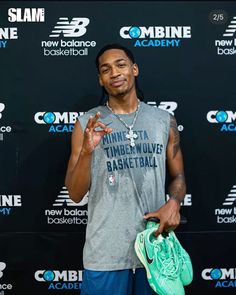 a man in grey shirt holding a green bag and wearing blue shorts on red carpet