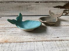 two small bowls sitting on top of a wooden table next to each other and one has a bird shaped bowl in the middle