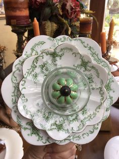 a person holding up a green and white flower shaped dish in front of a table