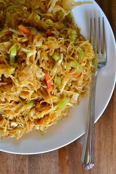 a white plate topped with shredded cheese and veggies next to a fork on top of a wooden table