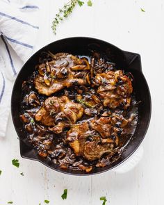 a skillet filled with meat and mushrooms on top of a white table next to a towel