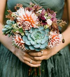 a woman in a green dress holding a bouquet of flowers and succulents