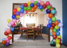 an arch made out of balloons is in the middle of a room with a table and chairs