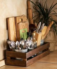 utensils and knives are in a wooden tray on the counter next to a potted plant