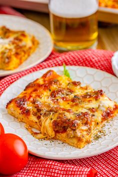 a slice of lasagna on a plate with tomatoes and beer in the background