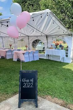 a sign that says class of 2012 with balloons in front of a tent and tables