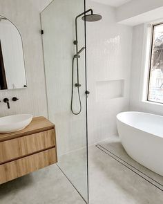 a white bath tub sitting next to a bathroom sink under a window in front of a mirror