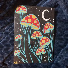 a painting of mushrooms and the moon on a black board with blue velvet material behind it