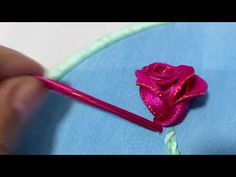 someone is stitching a rose on a blue piece of fabric with a pink needle