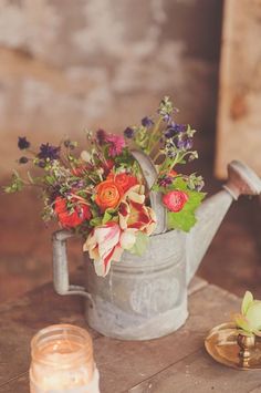 a watering can filled with flowers on top of a table