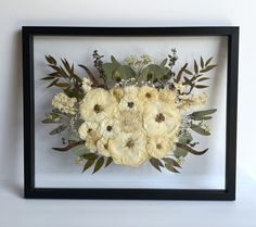 an arrangement of flowers is framed in a black frame on a white surface with green leaves