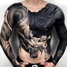 a man with dragon tattoos on his chest and arms is standing in front of a white wall