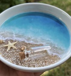 a hand holding a white bowl filled with sand and starfish