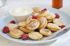 a white plate topped with pancakes covered in powdered sugar and raspberries next to a bowl of cream