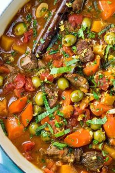 a bowl filled with stew and vegetables on top of a blue table cloth next to a wooden spoon