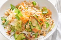 a white bowl filled with noodles, cucumbers and other vegtables