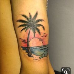 a woman's leg with a palm tree and sunset on the beach tattoo design