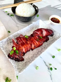 a plate with some meat and rice on it next to chopsticks, sauce and spoon