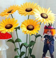 there is a doll standing next to some fake sunflowers in a glass vase