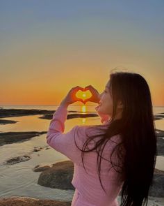 a woman standing on top of a beach holding a heart shaped object in front of her face