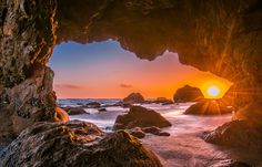 the sun is setting in an ocean cave with rocks and water on either side, as seen from inside