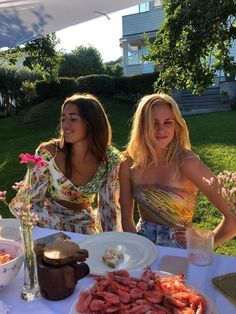 two women sitting at a table with food on it and one woman standing next to her