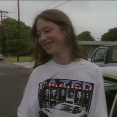 a woman standing in front of a white car and wearing a t - shirt with an image of the rolling stones on it