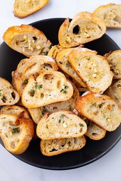 a black plate topped with slices of bread covered in cheese and herbs on top of a white table