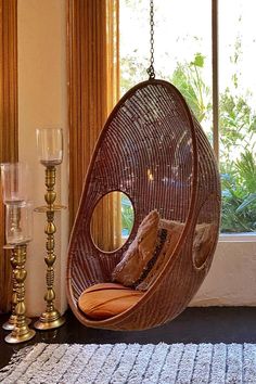 a hanging egg chair in front of a window with candles on the side and a candle holder next to it