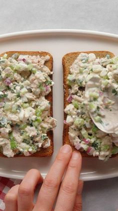 two pieces of bread with chicken salad on them and a hand reaching for the sandwich