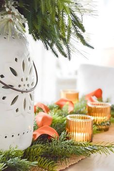 a table topped with candles and greenery next to a vase filled with pine cones