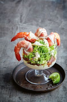 a salad with shrimp and lettuce in a glass bowl on a black plate