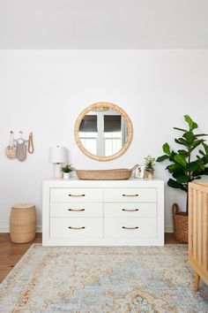 a white dresser sitting next to a mirror and potted plant on top of it