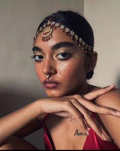 a woman in a red dress with gold jewelry on her head and hand near her face