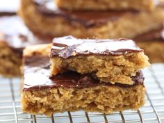 three pieces of chocolate - covered cookie bars cooling on a wire rack with more cookies in the background