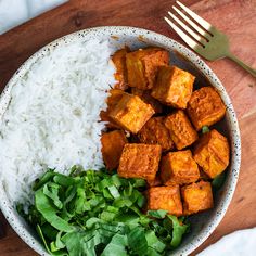 a white bowl filled with rice and tofu next to a green leafy salad