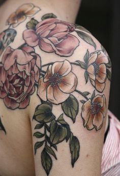 the back of a woman's shoulder with flowers and leaves tattooed on her arm