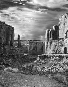 black and white photograph of rock formations in the desert with cloudy sky above them,