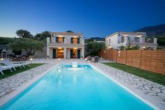 a house with a swimming pool in front of it at night, surrounded by lawn chairs