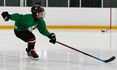 a young man skating on an ice rink wearing green jersey and black pants, holding a hockey stick