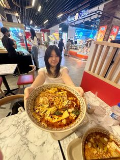 a woman sitting at a table with a large pizza in front of her and other food dishes on the table