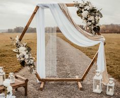 a wedding arch decorated with white flowers and greenery on the side of a road