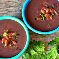 two blue bowls filled with soup sitting on top of a wooden table next to cilantro