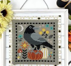 a cross stitch pattern with a black bird sitting on top of a pumpkin and flowers