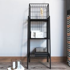 a bird cage sitting on top of a book shelf next to a white box and some candles