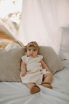 a baby sitting on top of a bed next to pillows