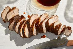 sliced pork on a plate next to a knife and sauce