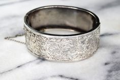 Antique sterling silver hinged bangle bracelet from the late Victorian Era. The front is hand engraved with swirling ivy leaves. The design extends a little bit to the back side of the bracelet for a little extra detail. Era: Victorian Markings: None Material: Sterling Silver (acid tested) Measurements: 24.5 mm wide 58mm x 46.2mm Condition: Good antique condition with minor wear from age. A few dings and dents on the back. Hinge works well. Safety chain is intact. Shipping is free in the United Formal Engraved White Gold Bangle, Antique Wedding Bracelets With Polished Finish, Heirloom Silver Engraved Bracelets, Etched Sterling Silver Bangle Bracelet For Wedding, Elegant Etched Cuff Bracelet For Anniversary, Elegant Silver Bangle With Engraving Option, Formal Engraved Antique Silver Bracelet, Engraved Sterling Silver Bracelet For Wedding, Silver Engraved Bracelets For Wedding